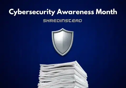 Photograph on a dark blue background with white text at the top reading, "Cybersecurity Awareness Month". Below that, silver text reads, "SHREDINSTEAD". In the center is a silver shield icon, and at the bottom is a large stack of white papers.