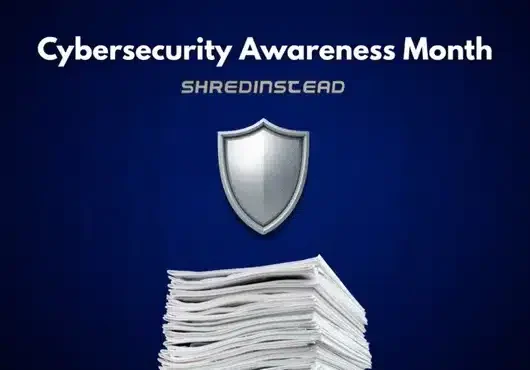 Photograph on a dark blue background with white text at the top reading, "Cybersecurity Awareness Month". Below that, silver text reads, "SHREDINSTEAD". In the center is a silver shield icon, and at the bottom is a large stack of white papers.